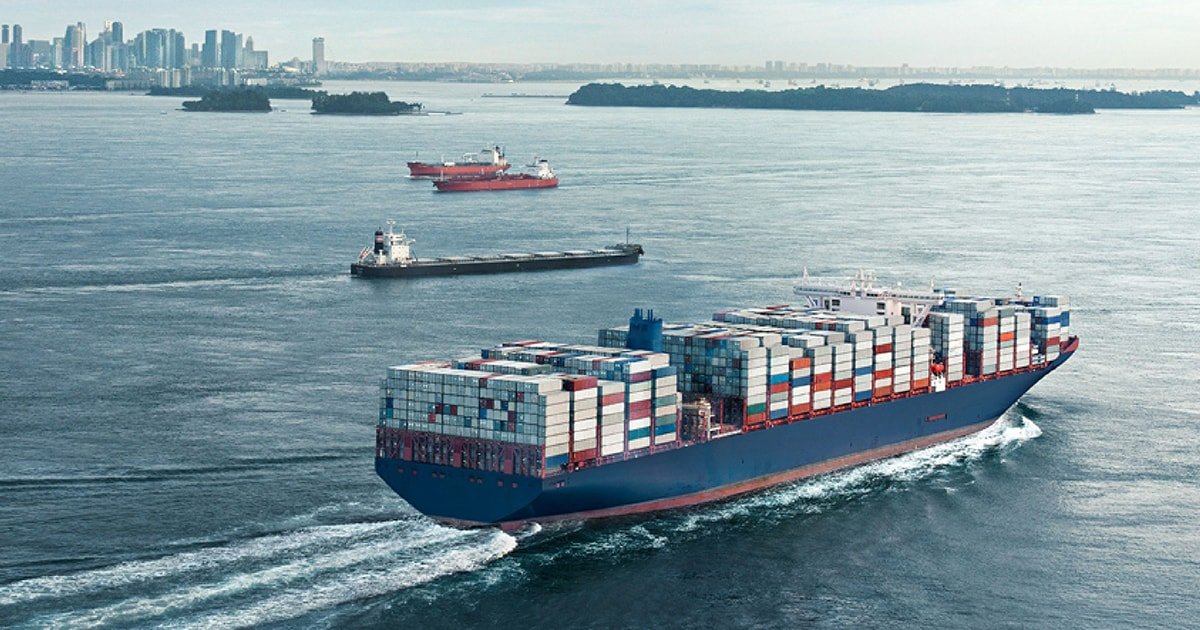 Large container ship sailing through open water with a distant skyline on the horizon.